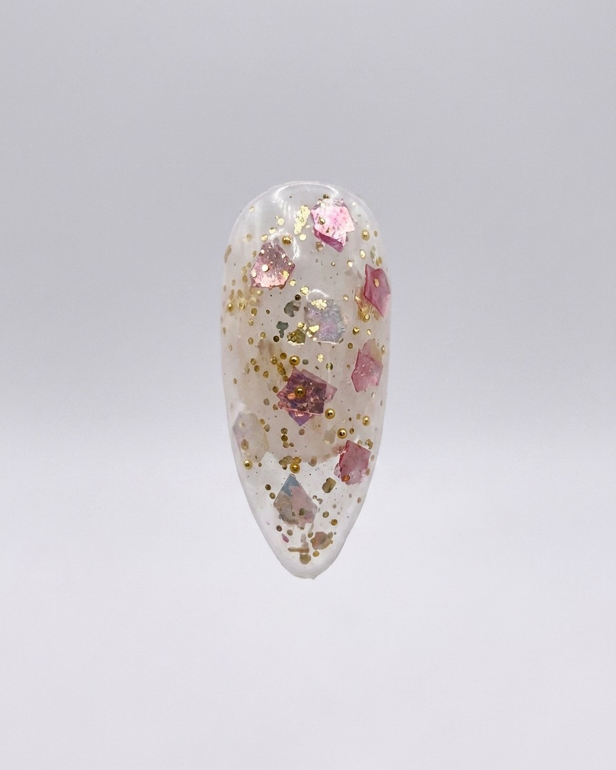 Ununghia press-on trasparente con fiocchi di glitter rosa e oro incorporati, isolata su sfondo grigio chiaro.