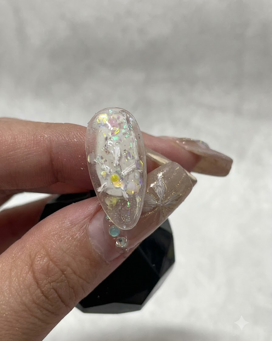 Primo piano di ununghia che mostra i primi tratti di gel plastico bianco che formano linizio di un disegno floreale.