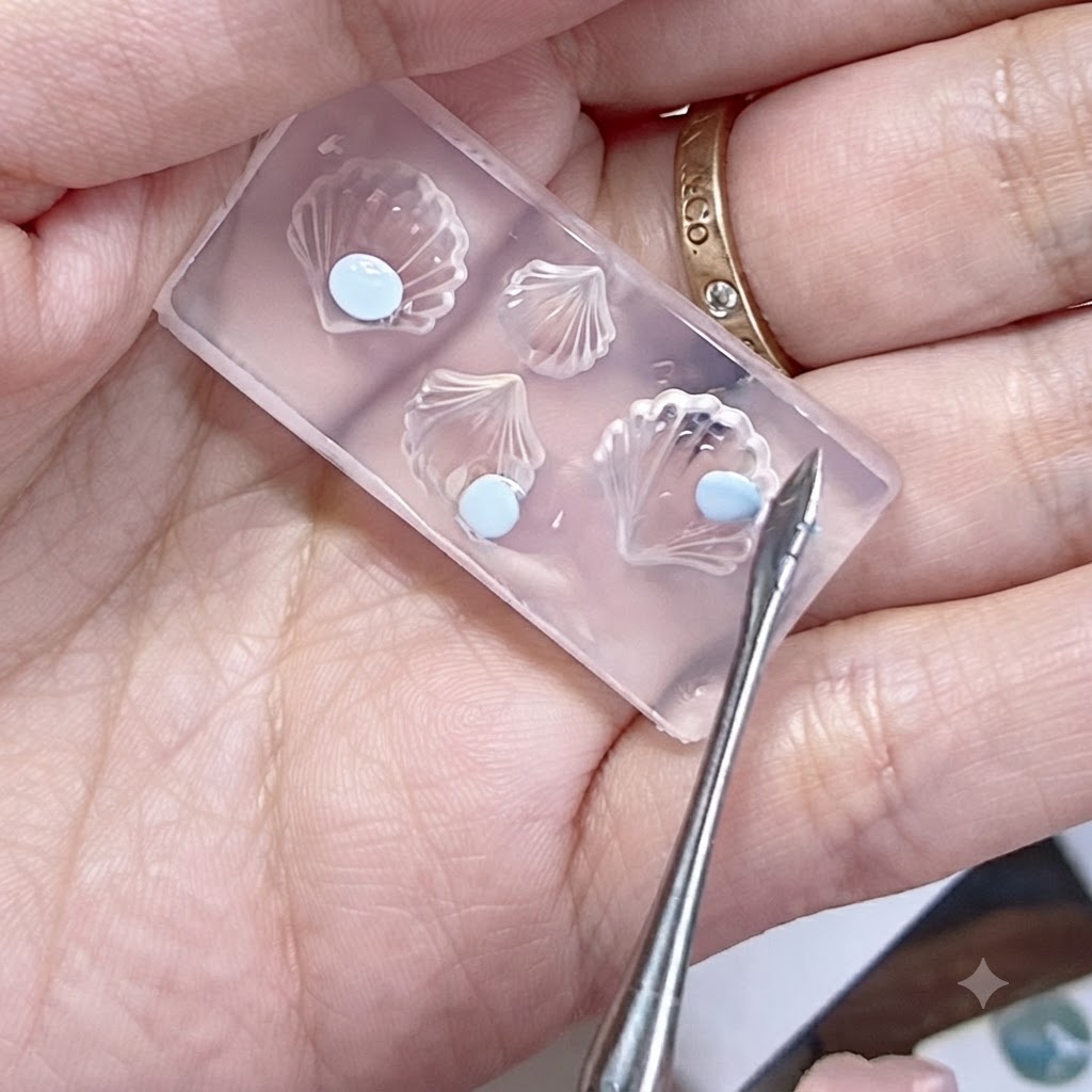 Uno stampo in silicone tenuto in mano con perle di gel blu appiattite e uno strumento di modellazione vicino.