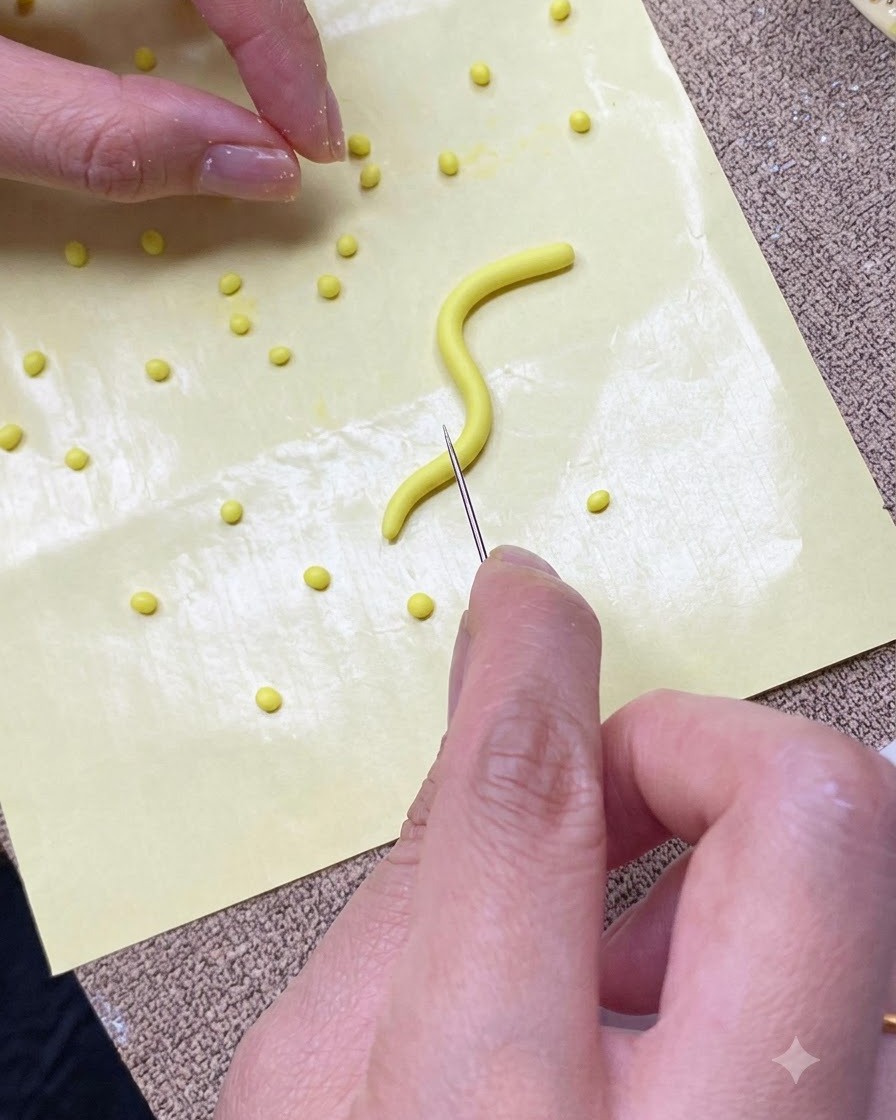 Un primo piano di mani che tagliano una striscia di gel giallo in piccole porzioni su un tappetino in silicone giallo usando uno strumento ad ago.
