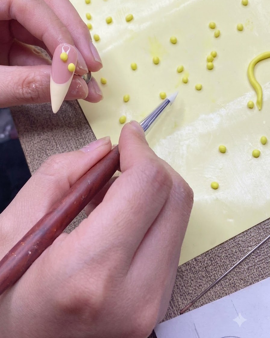 Una penna modellante in silicone che trasferisce una piccola pallina di gel giallo su una tip per unghie da pratica color carne.