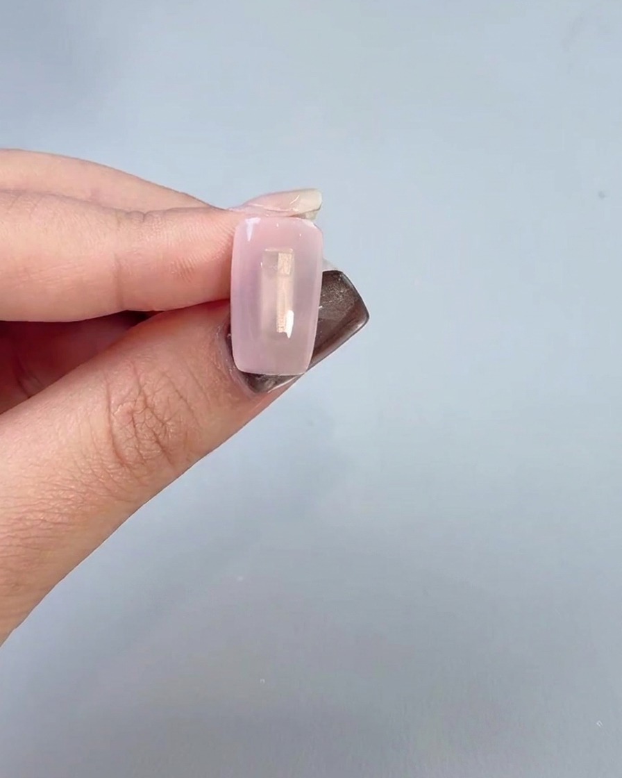 Primo piano di una mano che applica un gel base trasparente sulla superficie dellunghia con un pennello.