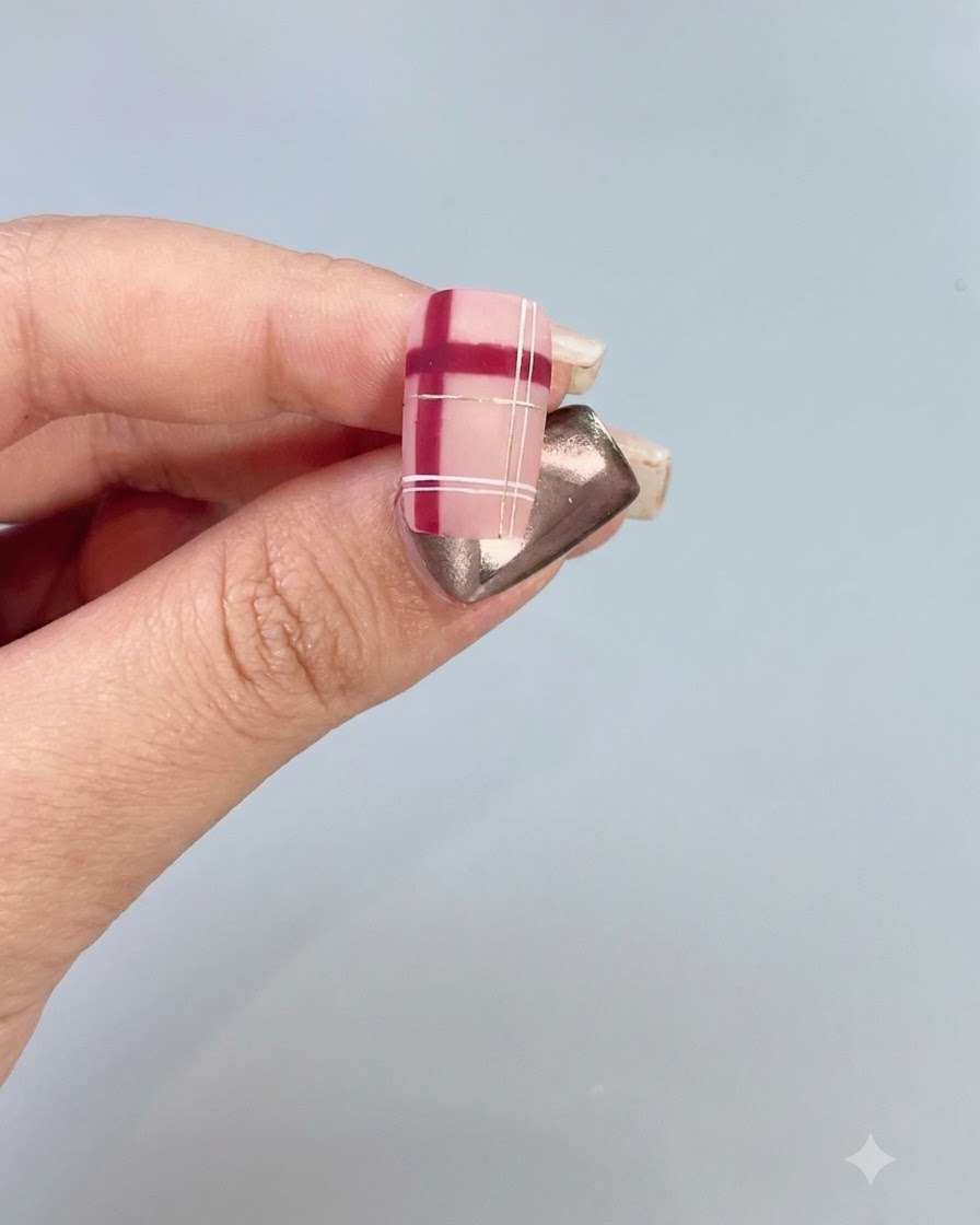 Primo piano di ununghia decorata con un motivo scozzese rosso e bianco con accenti dorati.