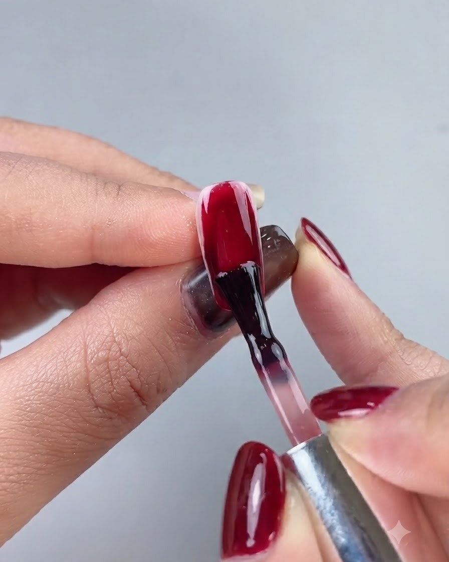 Un pennello per unghie che applica uno smalto gel rosso scuro bordeaux su unintera estensione dellunghia.