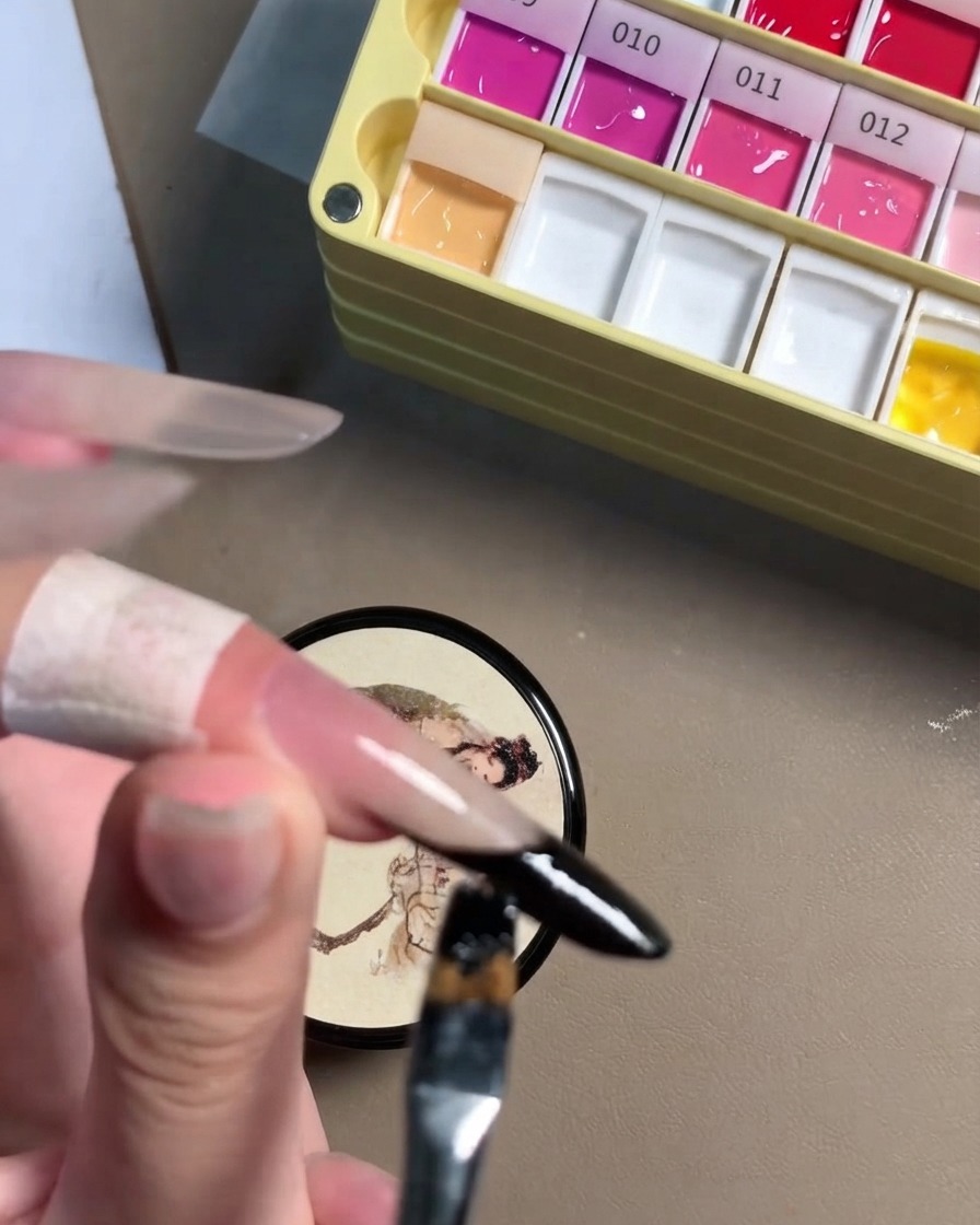 Una vista ravvicinata di un pennello di dettaglio che perfeziona la linea in gel nero sul bordo di ununghia stiletto.