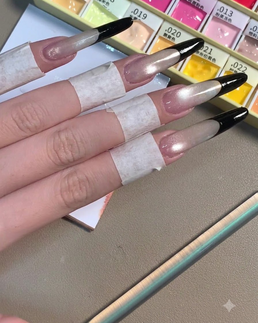 Quattro unghie stiletto lunghe che mostrano profonde French tips nere completate su una base grigia shimmer.