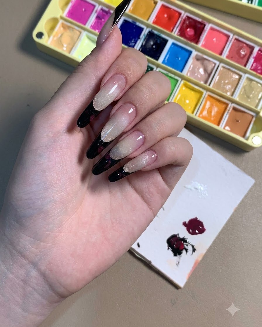 Una mano che mostra unghie stiletto con French tips nere e contorni di rose color prugna scuro.