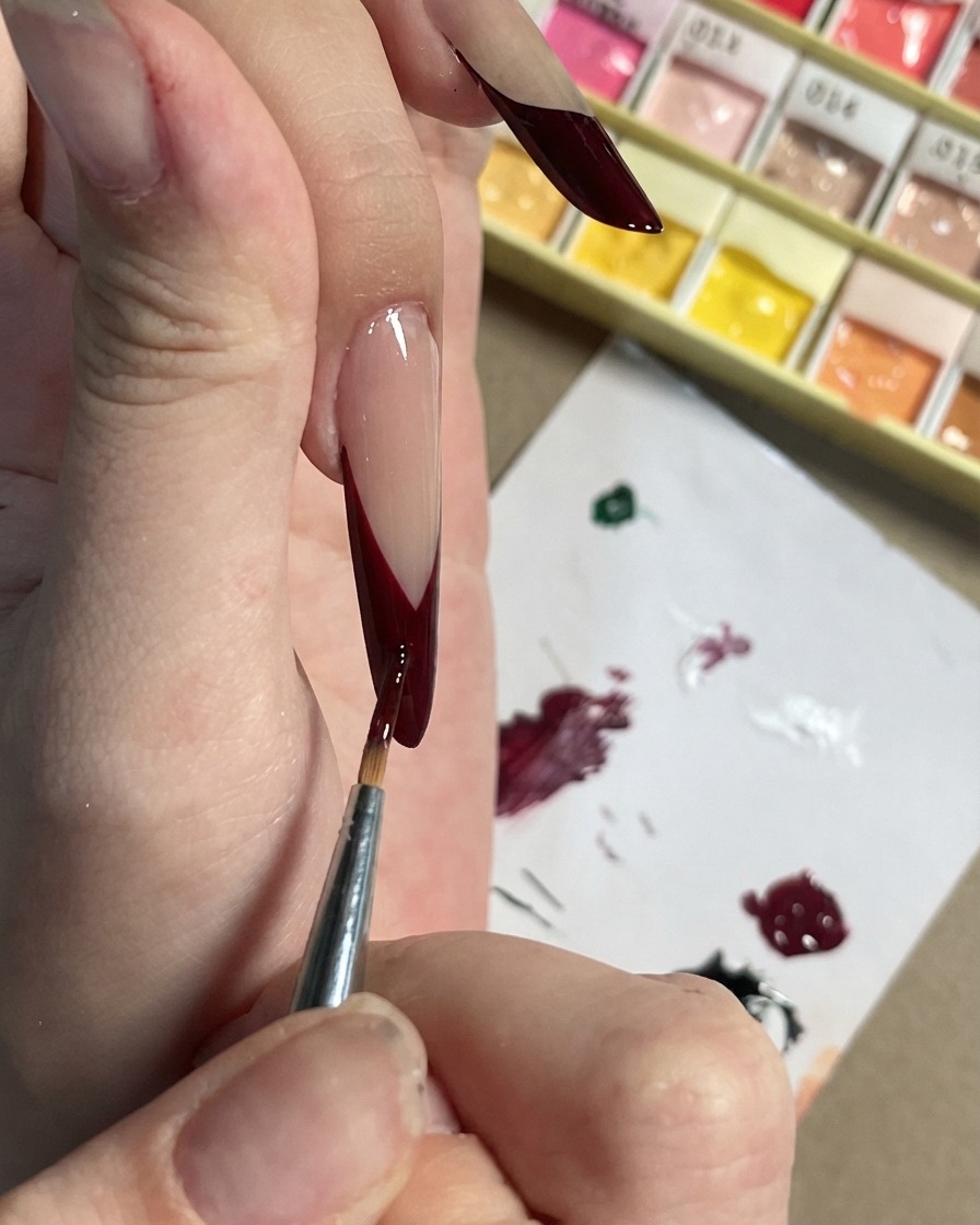 Un pennello fine che aggiunge piccoli accenti color prugna scuro e forme di petali su una French tip nera.