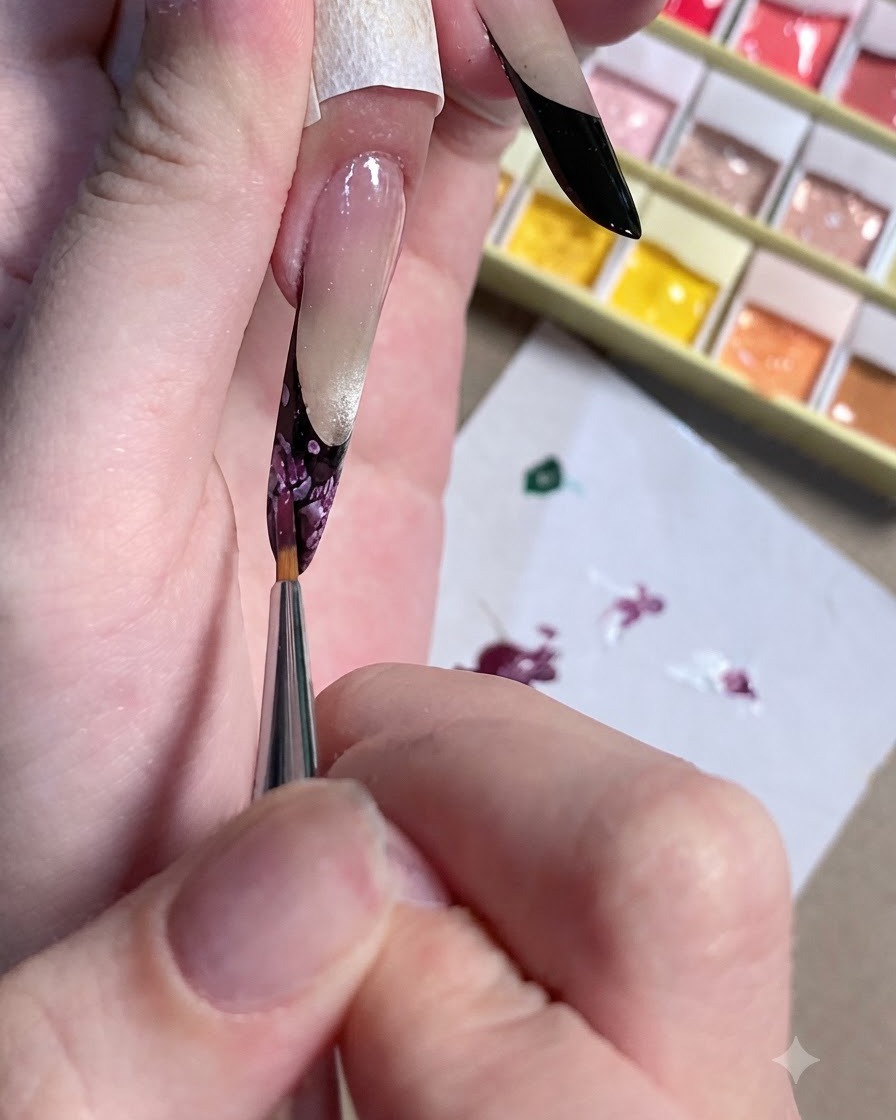 Un primo piano di un pennello di dettaglio che rifinisce il centro scuro di un design floreale per unghie.