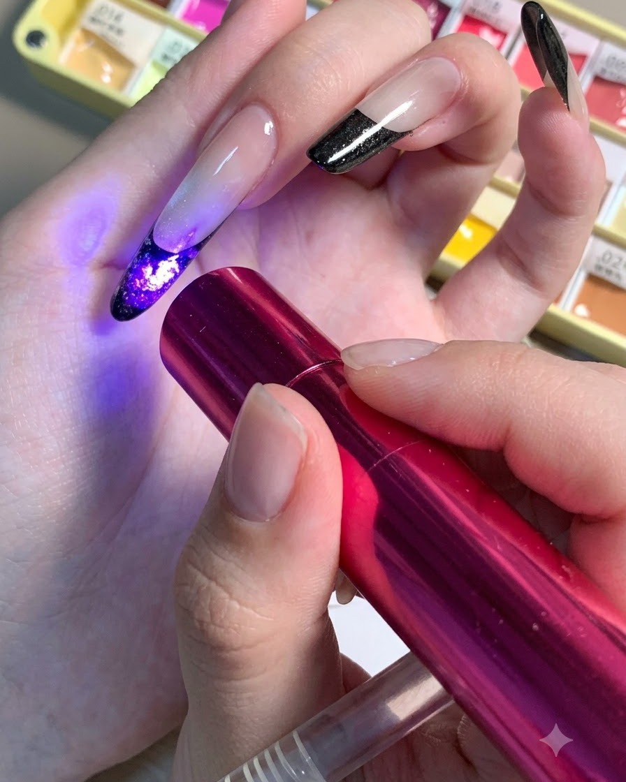 Una mini lampada UV/LED rossa tenuta sopra ununghia per polimerizzare i dettagli del centro scuro di un design floreale.