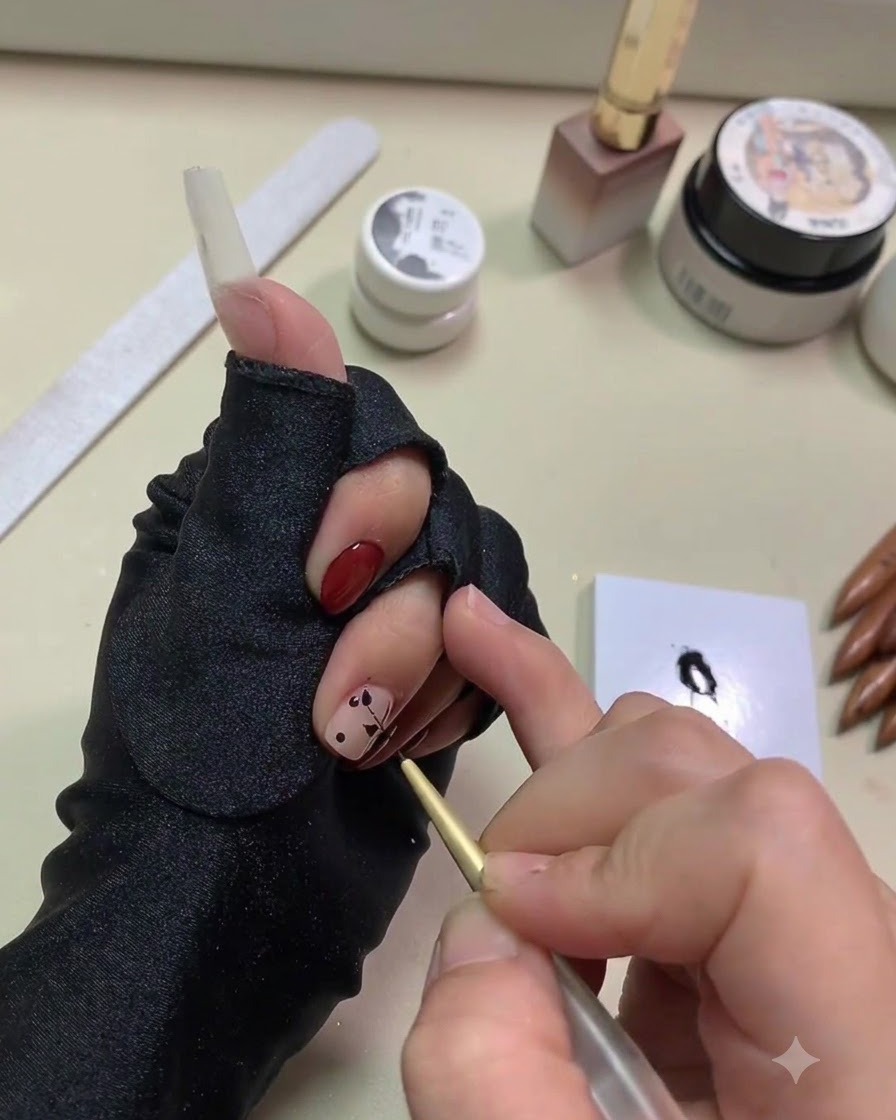 Primo piano di una mano che utilizza un pennello liner dorato fine per tirare il gel nero in forme di foglie da punti su ununghia con base nude.
