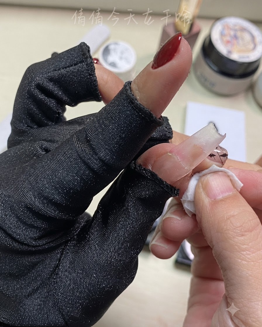 Primo piano di una mano che pulisce un dito con un pad detergente vicino a una nail art preparata.