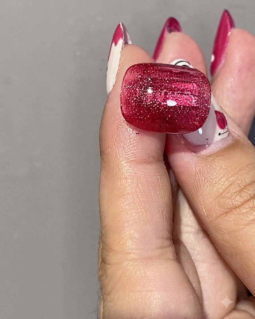 Primo piano di una mano che tiene un magnete cilindrico argentato vicino a ununghia in gel cat eye rosso lucido per modellare i riflessi magnetici.