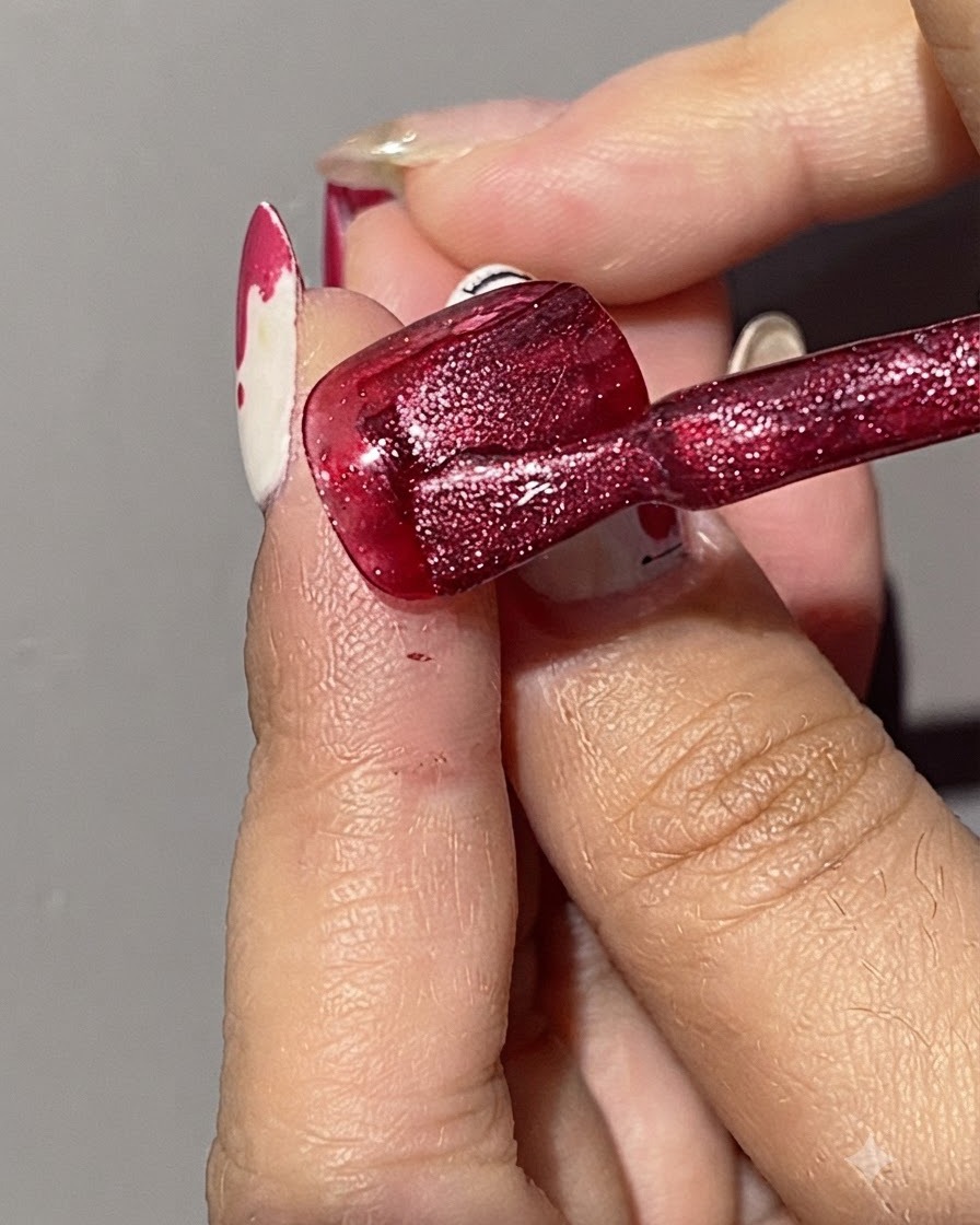 Un pennello che applica una seconda passata di smalto gel cat eye rosso scintillante su ununghia già dipinta di rosso.