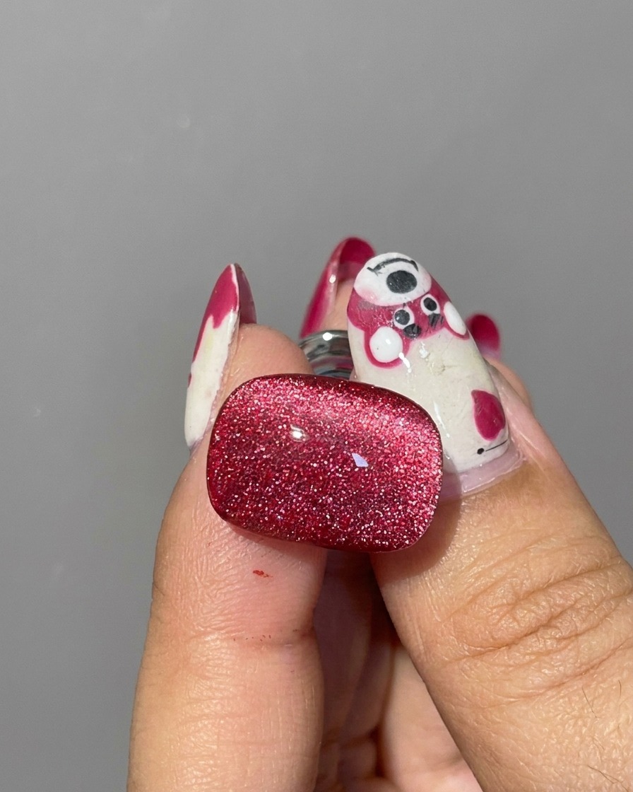 Primo piano di un magnete cilindrico argentato tenuto vicino ai bordi di ununghia in gel cat eye rosso non polimerizzato per spostare le particelle di glitter.