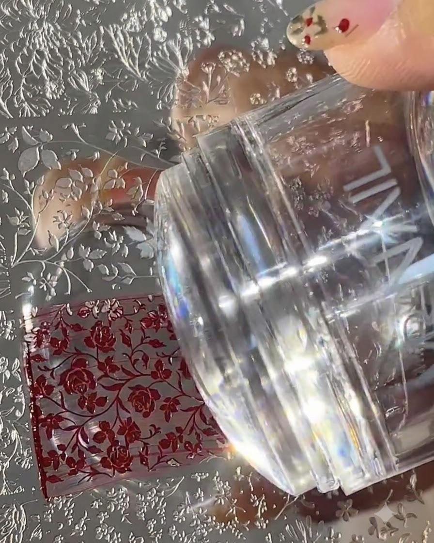 Uno stampino per unghie in silicone trasparente premuto su una piastra metallica per stamping incisa e riempita con motivi floreali rossi.