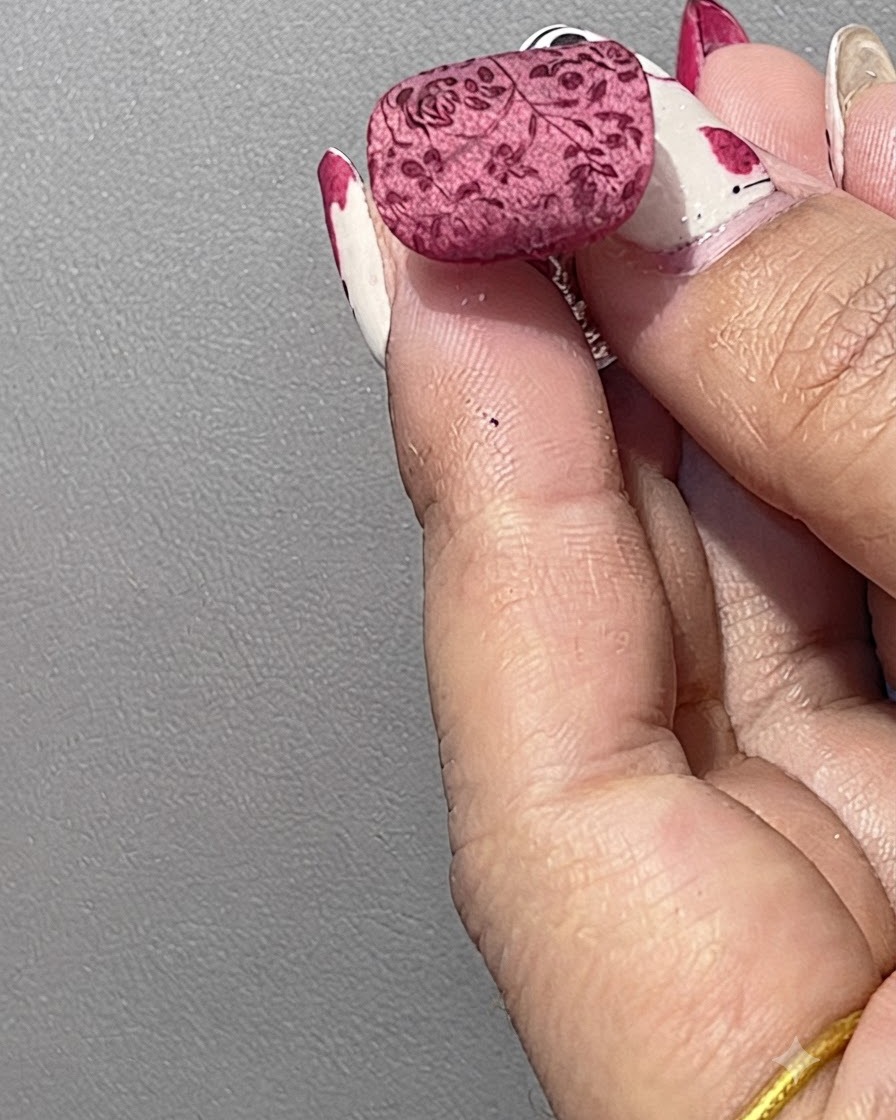Ununghia curata con un motivo floreale rosso stampato che viene leggermente ricoperta di polvere di cristallo bianca usando una spatola.