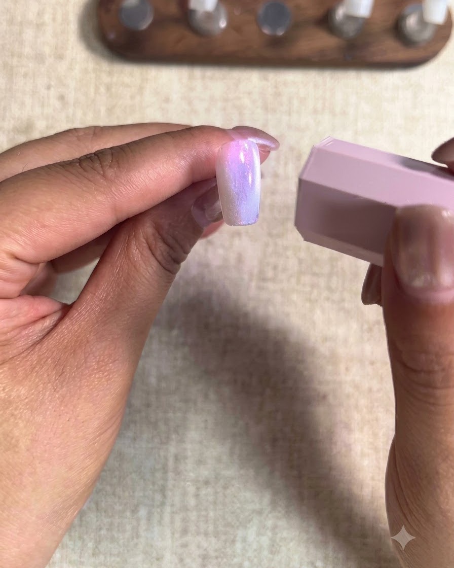 Primo piano di un pennello che applica uno smalto gel nude color pesca sullunghia del dito indice.