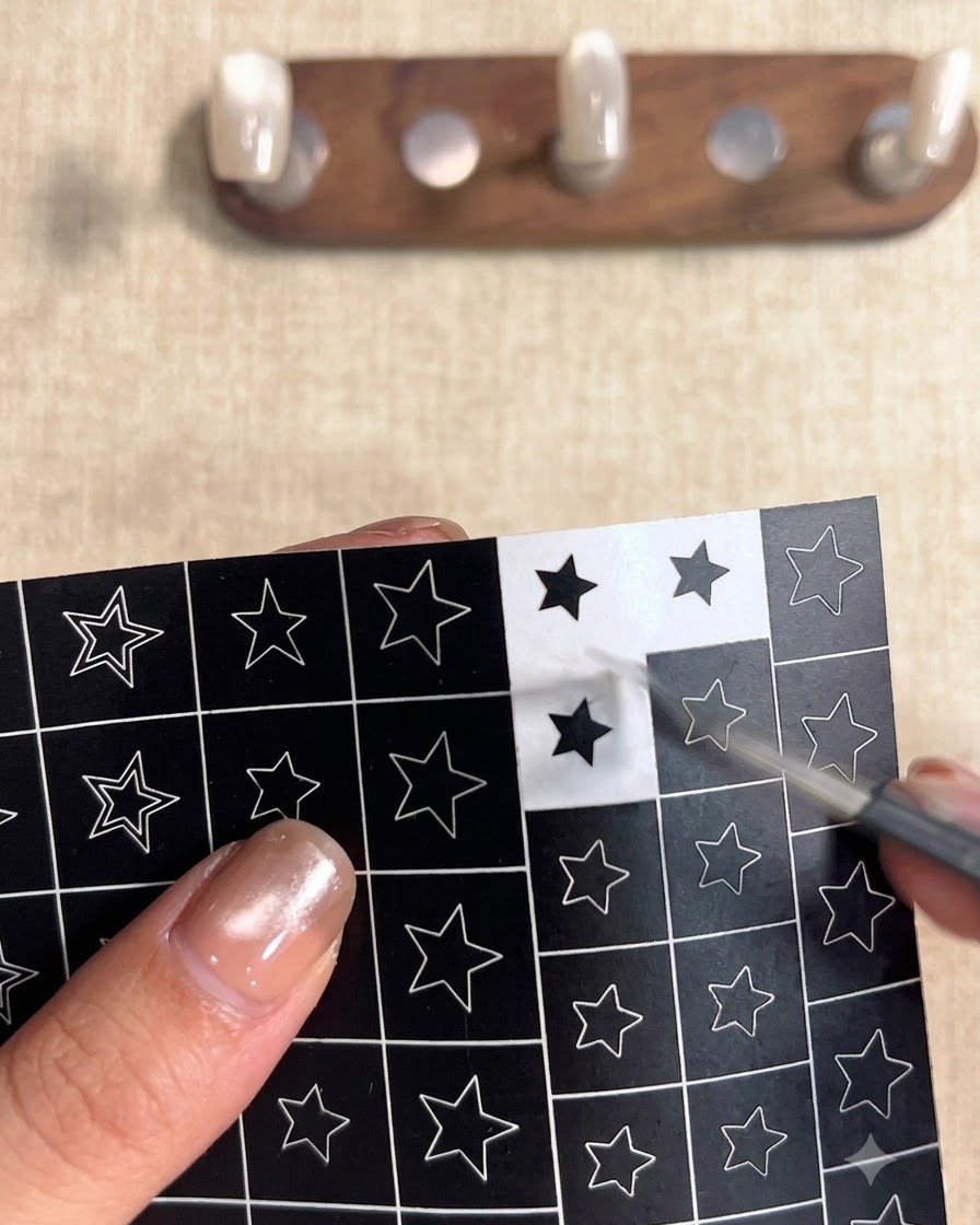 Una mano che usa delle pinzette per staccare un adesivo quadrato nero con una stella vuota ritagliata da un foglio di design a stella.
