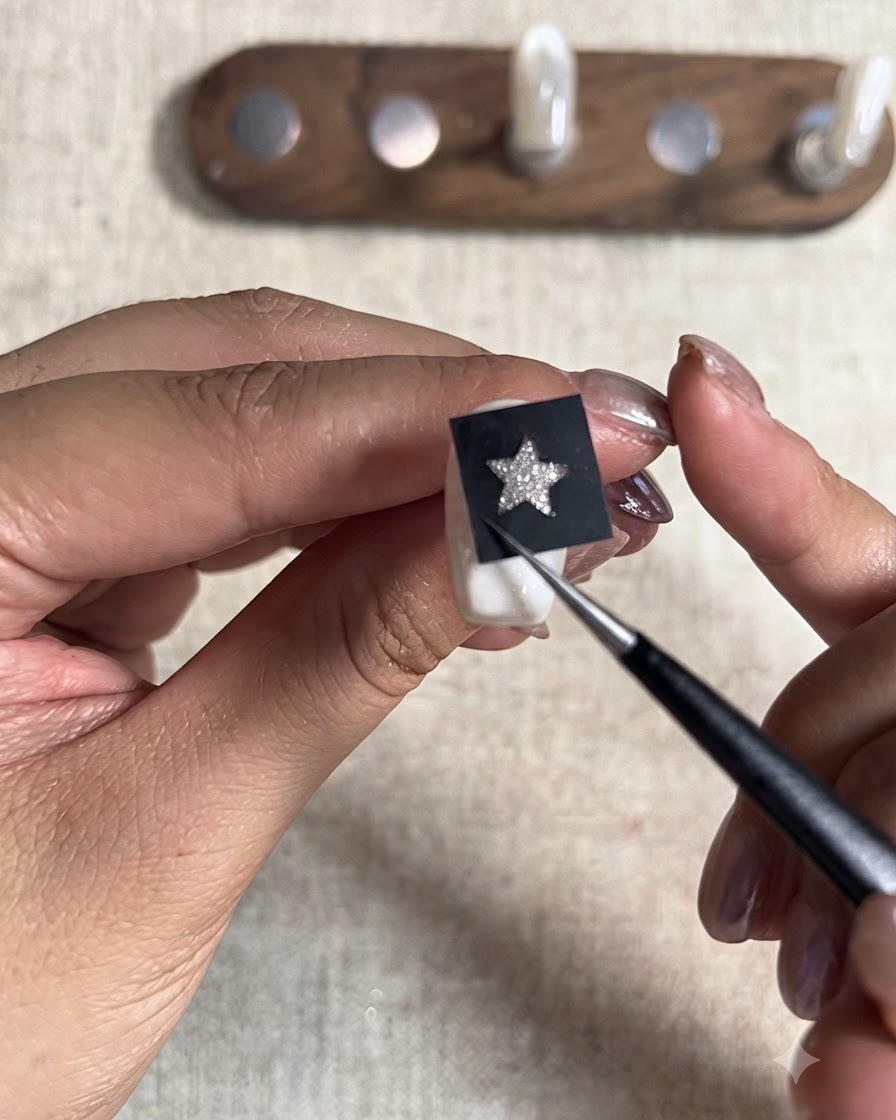 Uno strumento a punta che preme saldamente verso il basso su uno stencil a stella nero posizionato sopra una tip smaltata.