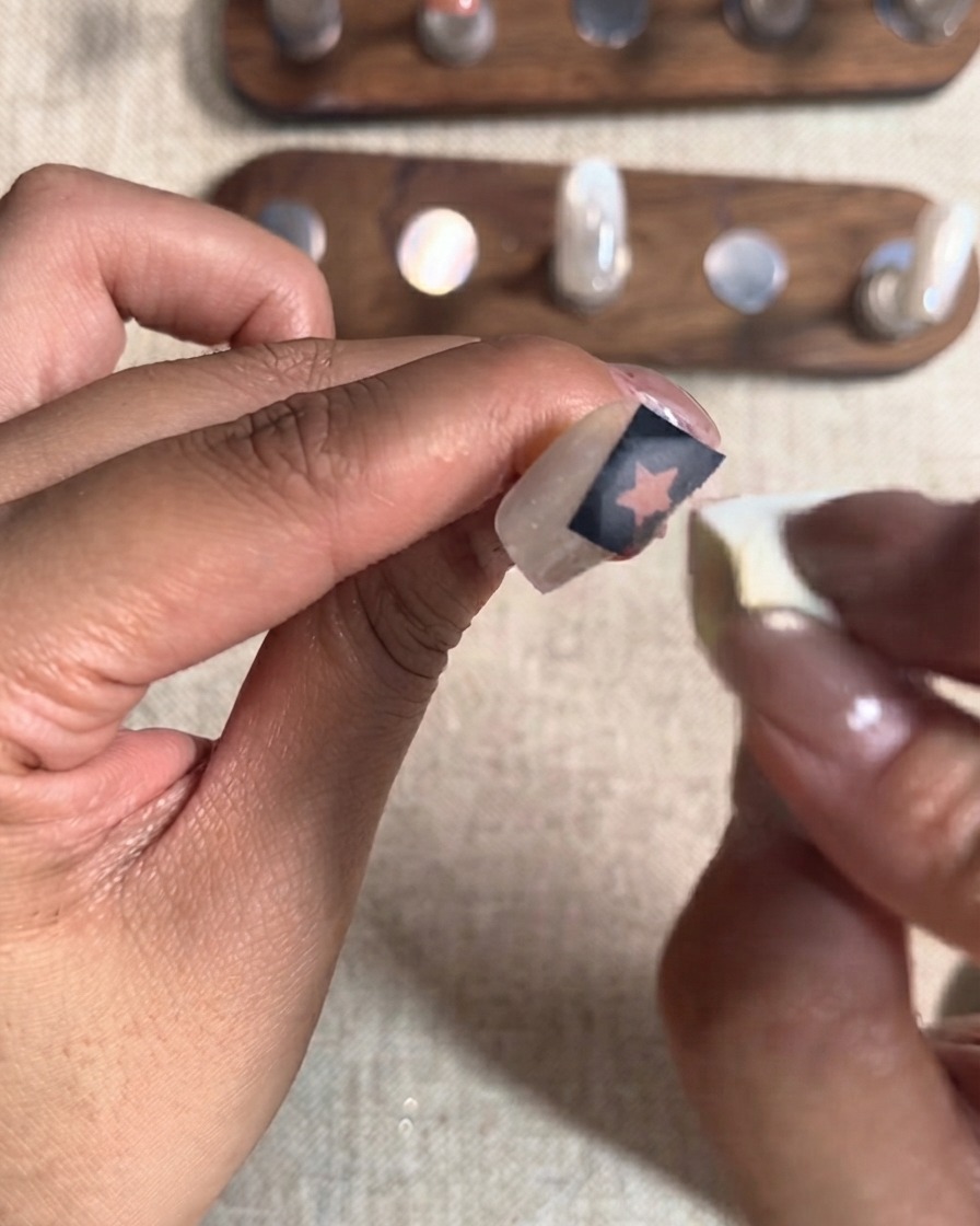 Una piccola spugnetta cosmetica che tampona un secondo strato di gel rosso su un adesivo a forma di stella ritagliata su ununghia.