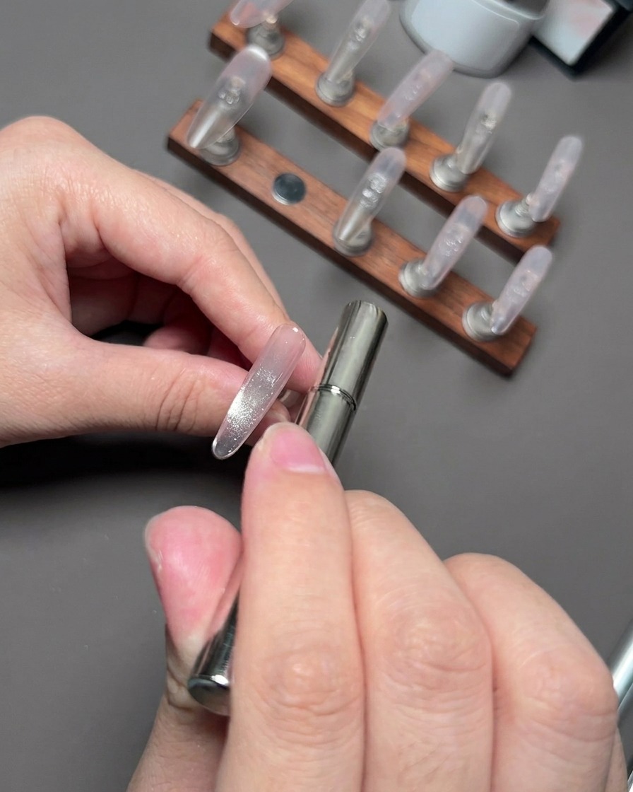 Una bacchetta magnetica che fluttua vicino a ununghia per raccogliere e modellare le particelle riflettenti cat eye.