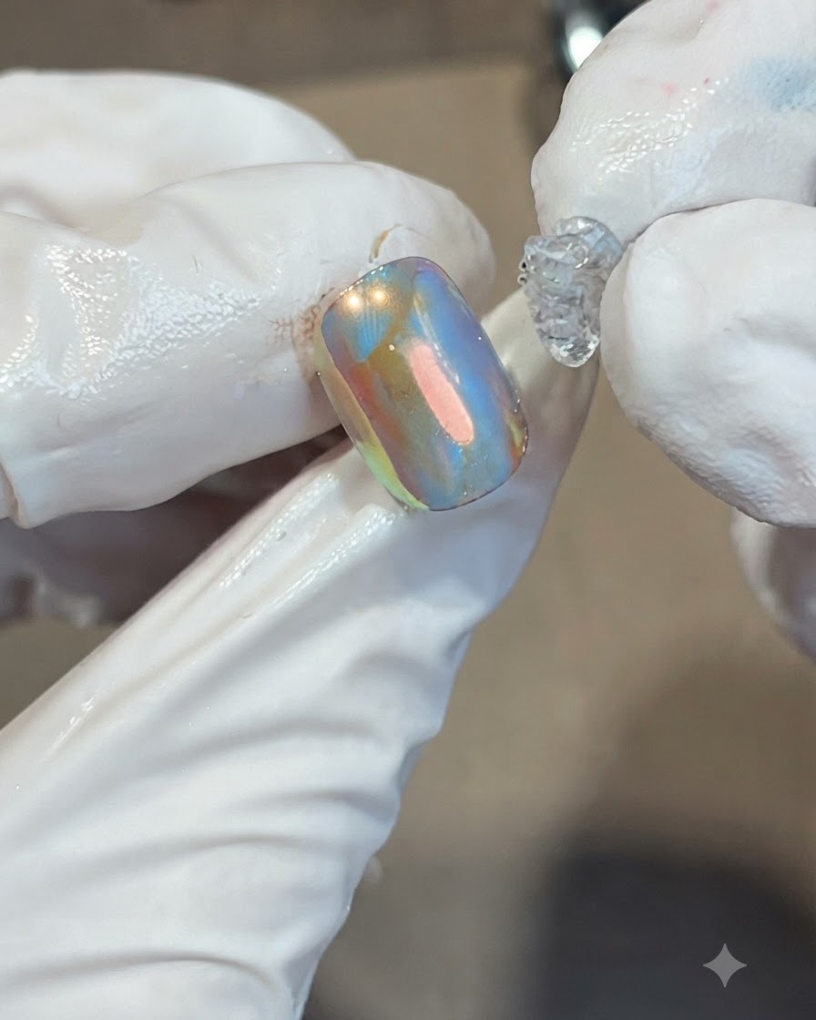 Il posizionamento di una goccia di gel morbido trasparente e denso al centro di ununghia iridescente arancione e blu.
