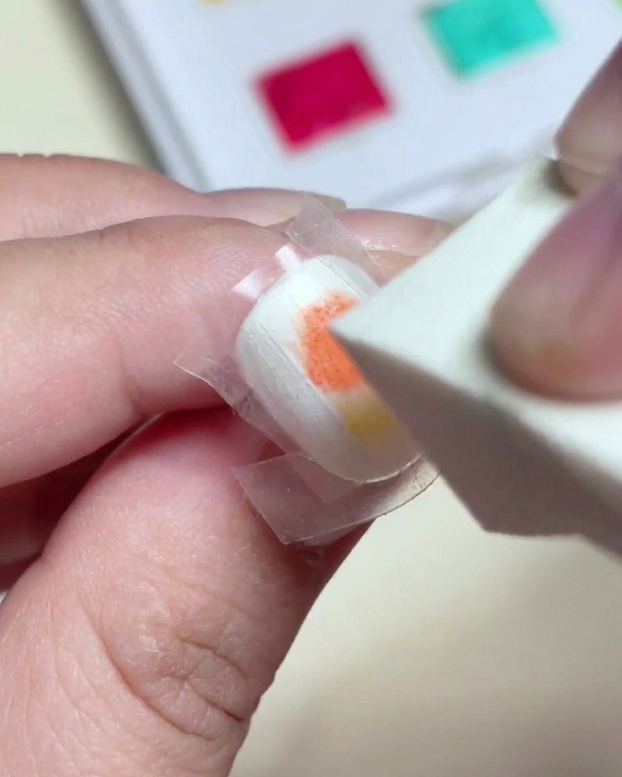 Una spugnetta per trucco che picchietta delicatamente sul gel rosso e giallo bagnato per creare un gradiente perfetto sullunghia.