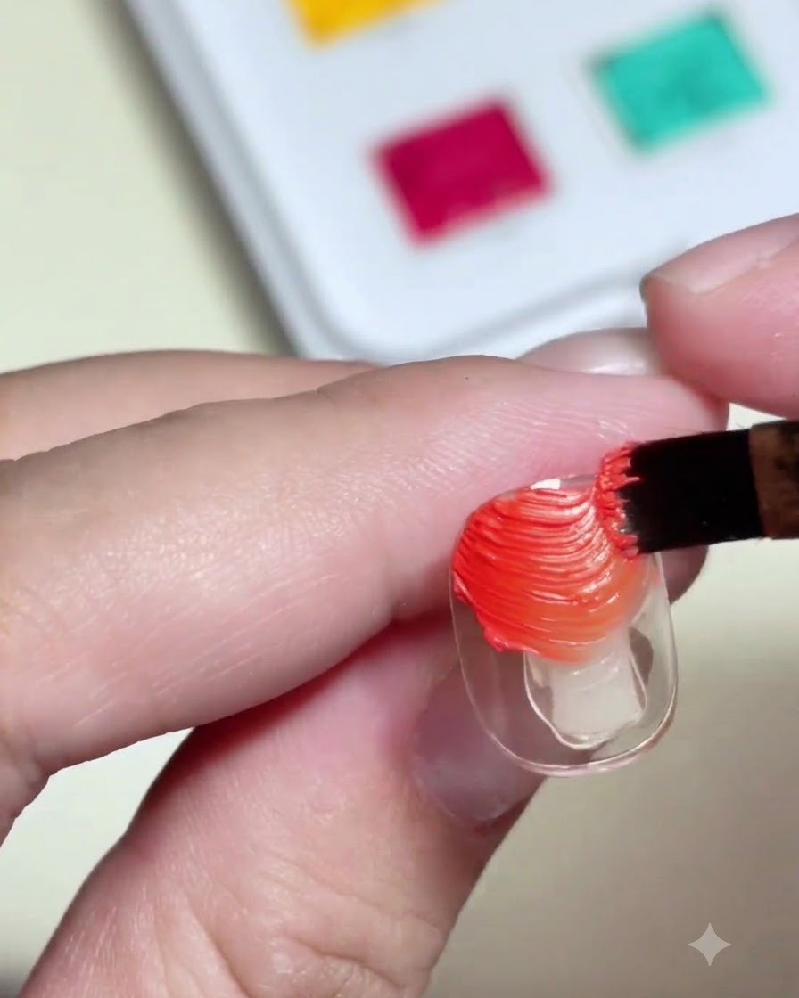 Un pennello per unghie che applica gel pittorico materico arancione e giallo su una tip trasparente.