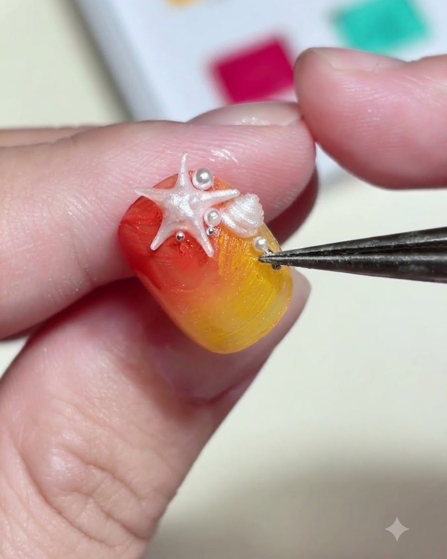 Un paio di pinzette che posizionano minuscole perline bianche e borchie metalliche attorno a un charm a forma di stella marina 3D su ununghia.