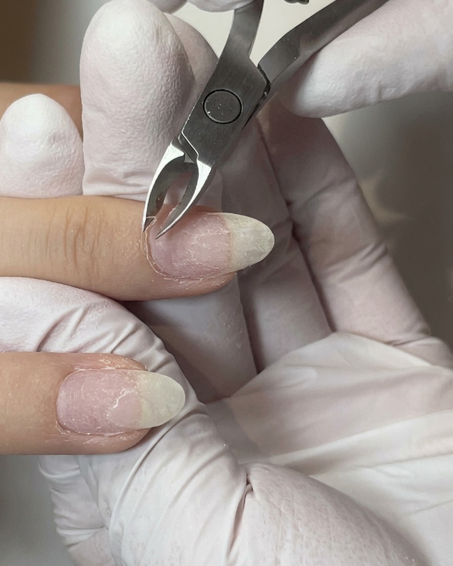 Forbicine per cuticole in metallo che tagliano con cura la pelle in eccesso attorno al girocuticola di un dito preparato.