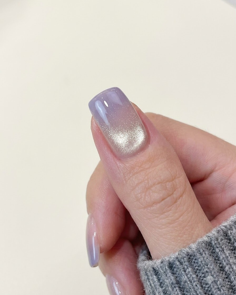 Ununghia completata con effetto cat-eye e sfumatura viola che mostra una fascia di luce brillante e scintillante vicino al bordo posteriore.