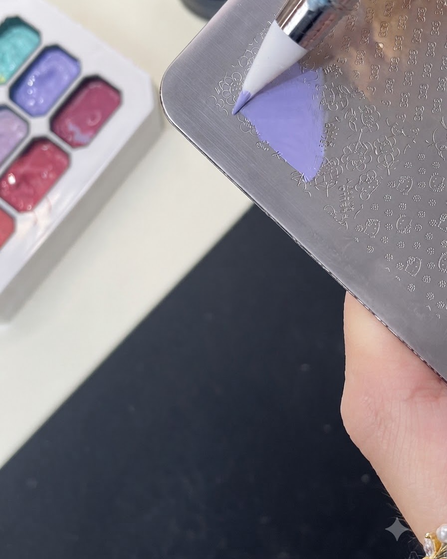 Un pennello che applica il gel colorato viola sopra un motivo inciso di Hello Kitty su una piastra da stampa in metallo.