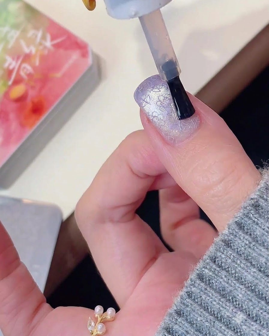 Un pennello per unghie che applica il top coat su un design di unghie viola cat-eye e stampato.
