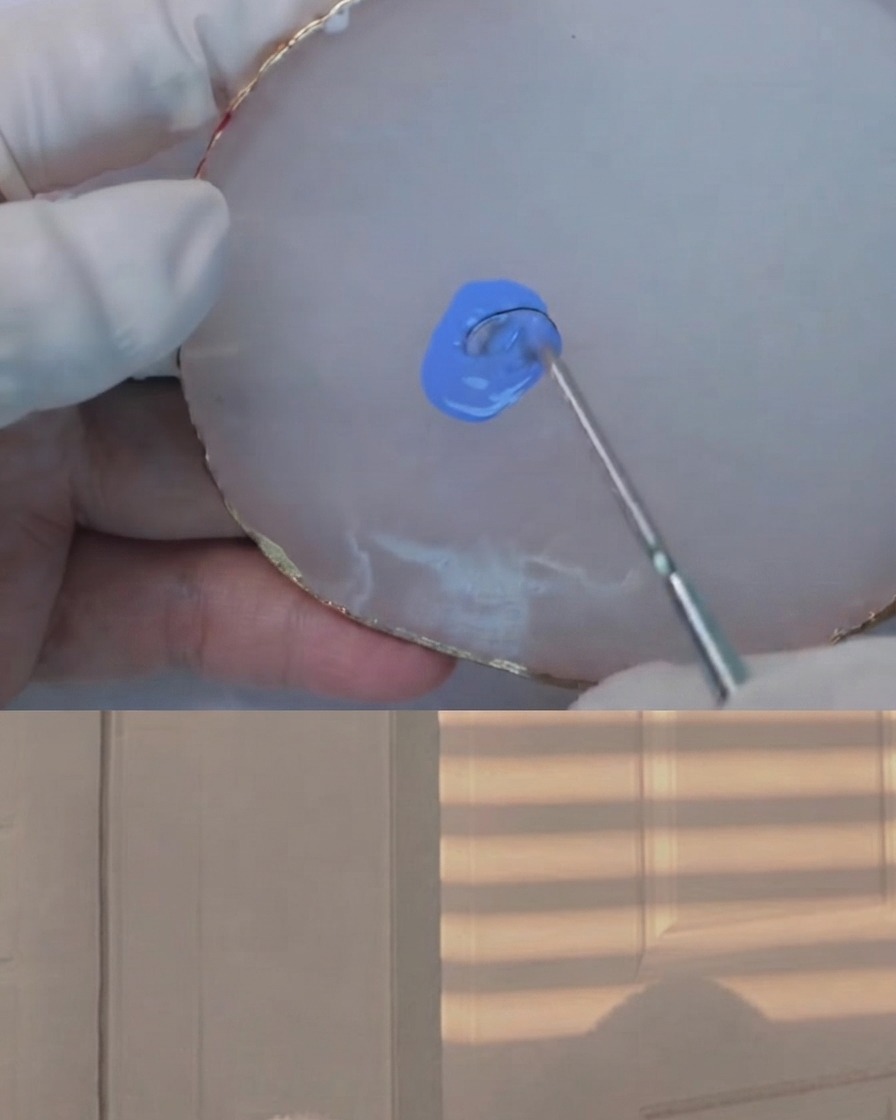 Uno strumento di miscelazione che sfuma una quantità minima di gel scuro in una miscela di azzurro chiaro su una tavolozza in agata bianca.