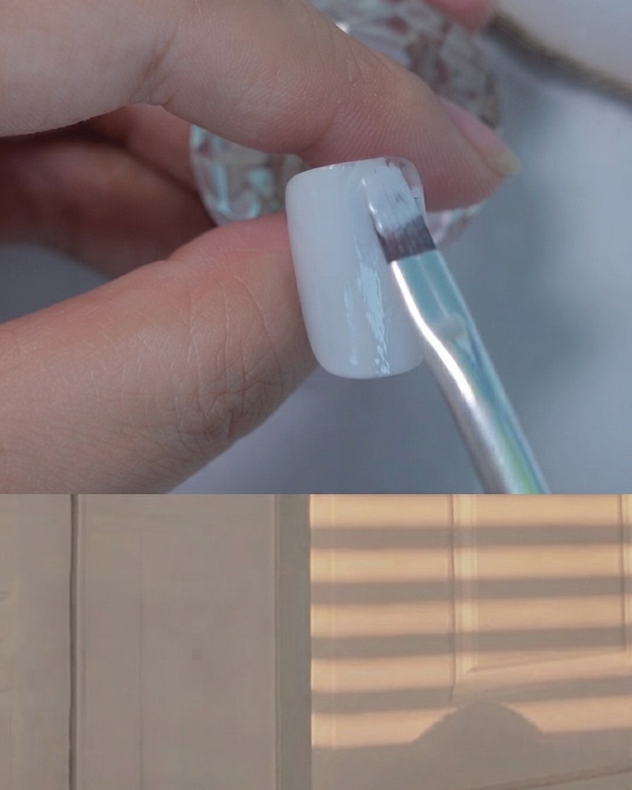 Un pennello per gel piatto che applica un sottile strato uniforme di smalto gel grigio chiaro su ununghia di supporto per esposizione.