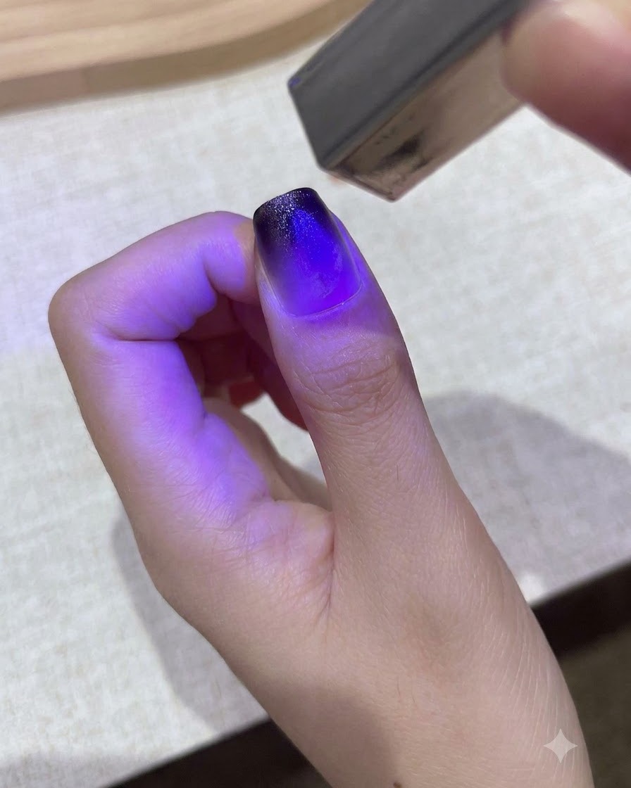 Una piccola lampada UV/LED portatile viola polimerizza un design in gel sfumato su ununghia del pollice.