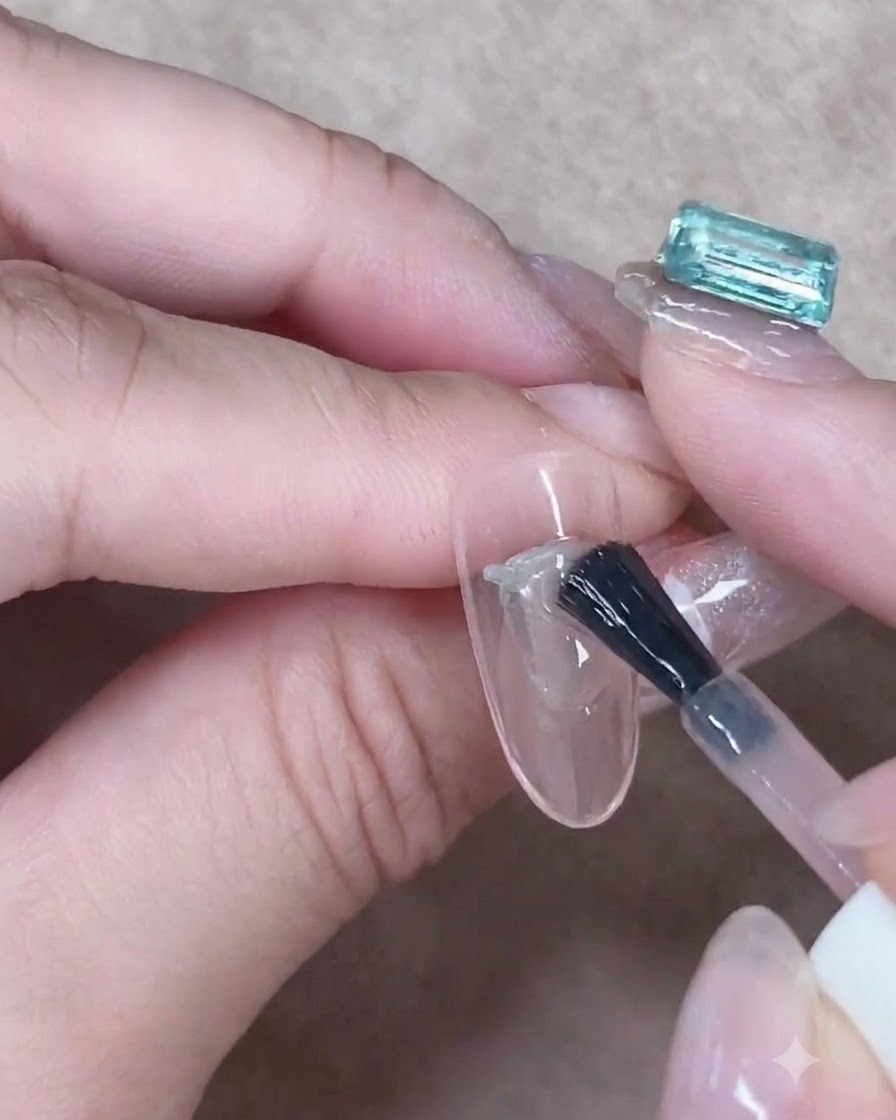 Un pennello da gel che stende accuratamente uno strato di gel nude traslucido lungo il centro di ununghia a mandorla.