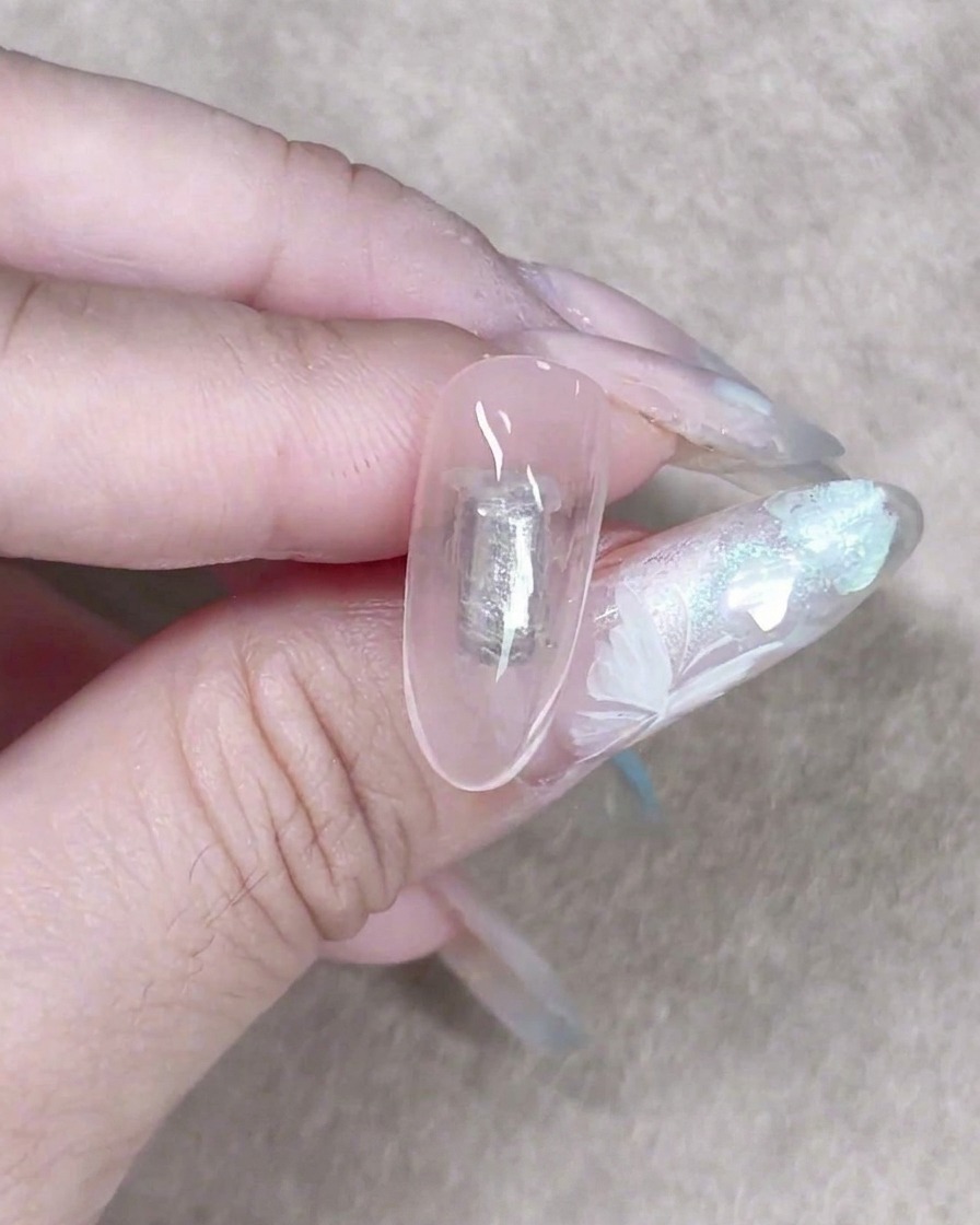 Una piccola spugnetta per make-up che tampona delicatamente un gel lattiginoso trasparente su ununghia per creare uno sfondo morbido e sfumato.