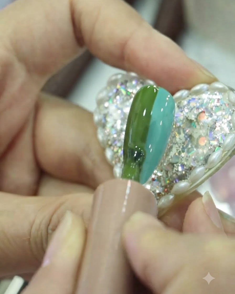 Un pennello piatto che sfuma delicatamente la sezione centrale dove il gel verde e teal si incontrano sullunghia.