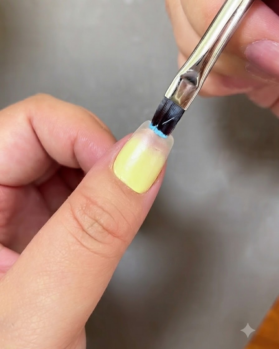Un pennello per nail art che applica il gel azzurro sulla punta di ununghia.