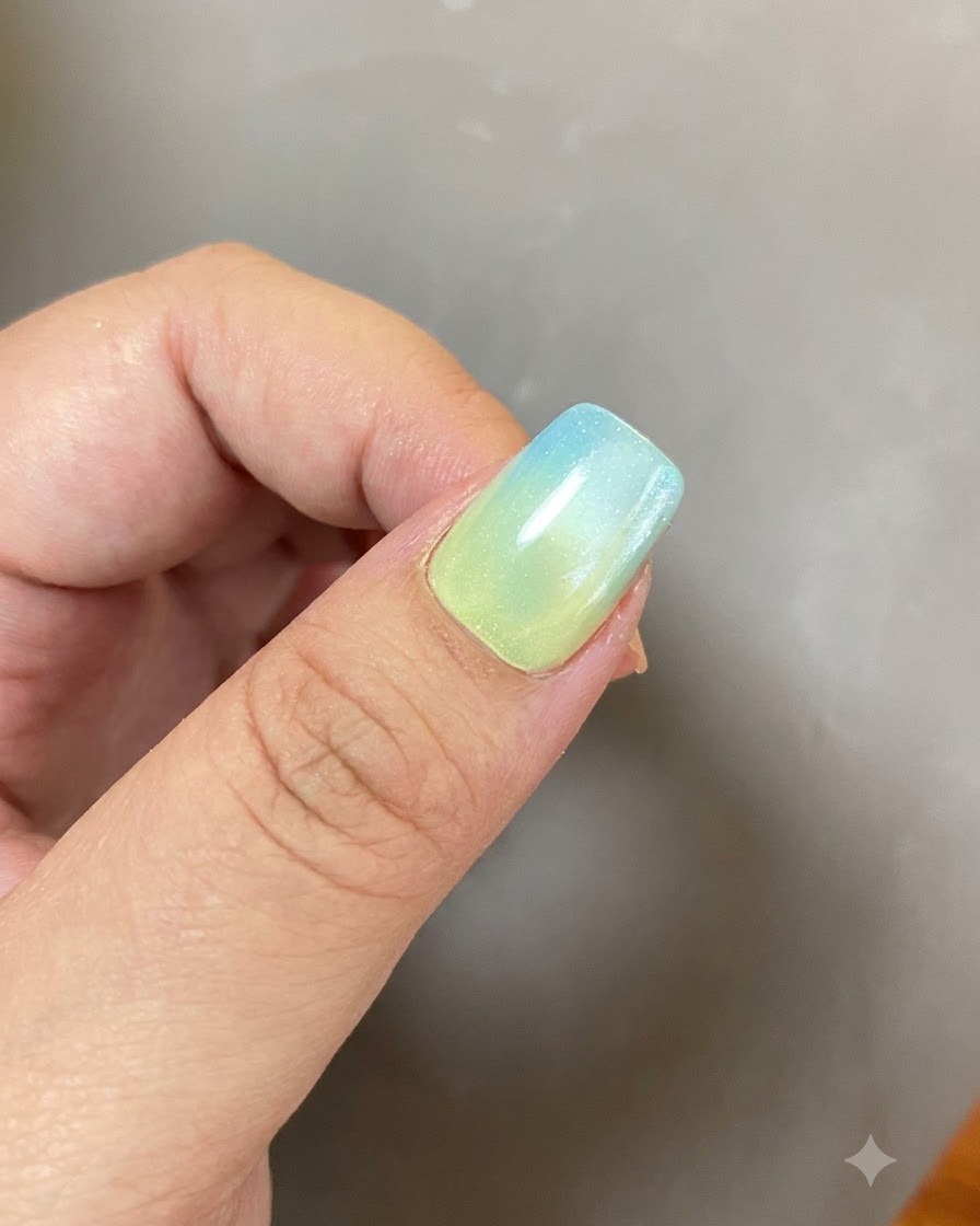 Una manicure in gel completata con sfumatura blu e gialla e un design ad anello luminoso sotto una luce soffusa.