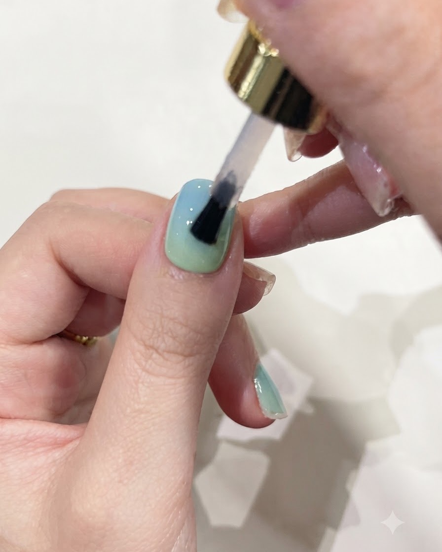 Un pennello applica un gel costruttore trasparente sopra ununghia colorata con gradiente.