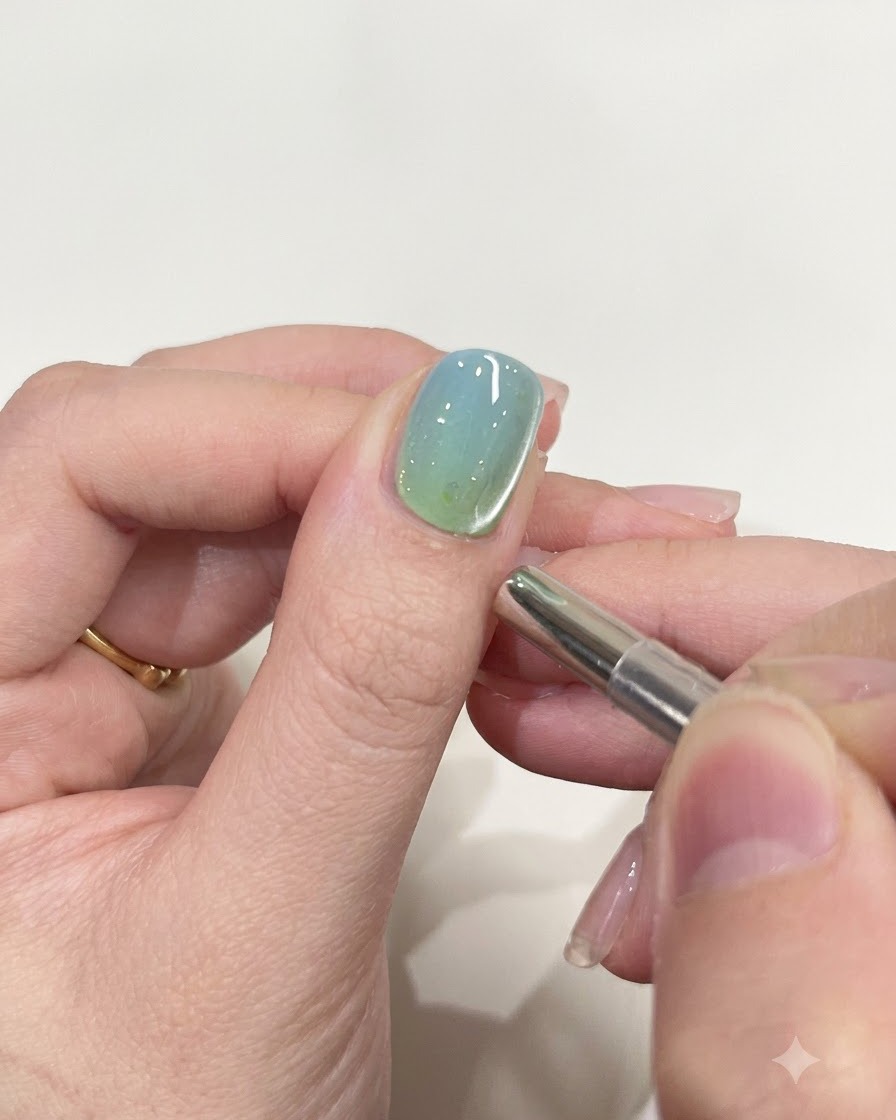 Un piccolo strumento magnetico cilindrico sospeso vicino al bordo di ununghia lucida dipinta in gel.