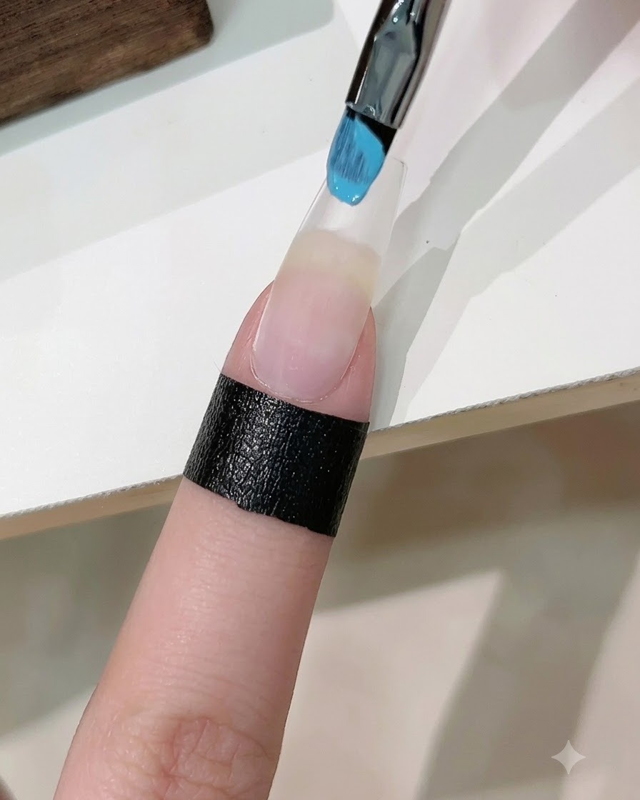 Una spugnetta con smalto gel blu e bianco che tampona una sfumatura su ununghia artificiale allungata.