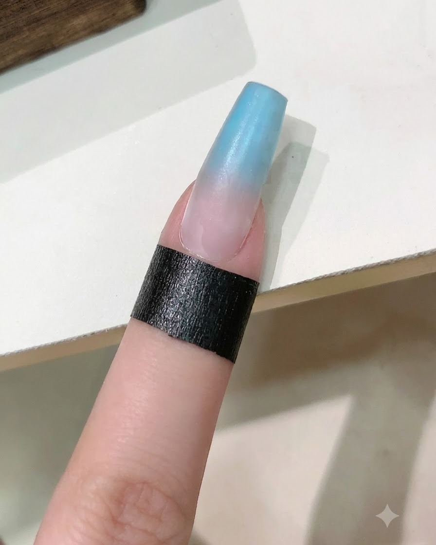 Un pennello da unghie che applica uno strato di gel rinforzante trasparente sopra lunghia sfumata di blu e rosa.