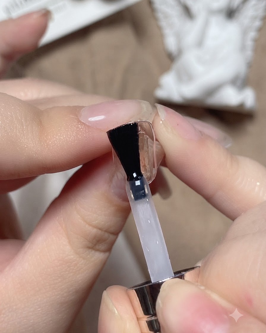 Un pennello da unghie applica una base coat trasparente su una tip di prova.