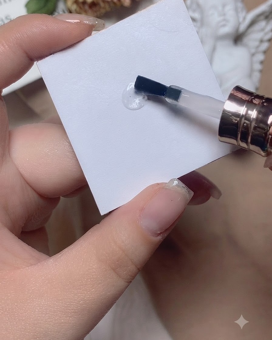 Un pennello lavora una goccia di base coat avanti e indietro su una superficie bianca della tavolozza.