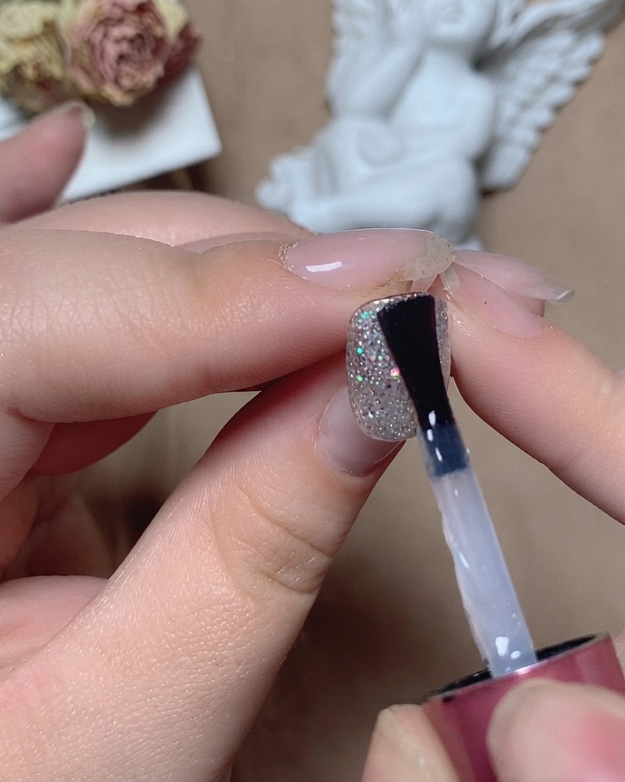 Un pennello applica un top coat livellante trasparente su ununghia glitterata ruvida sotto la luce dello studio.