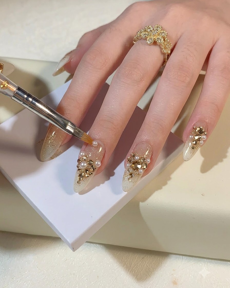 Una pinzetta o uno strumento di precisione posiziona piccole perle e strass oro champagne su ununghia glitterata.